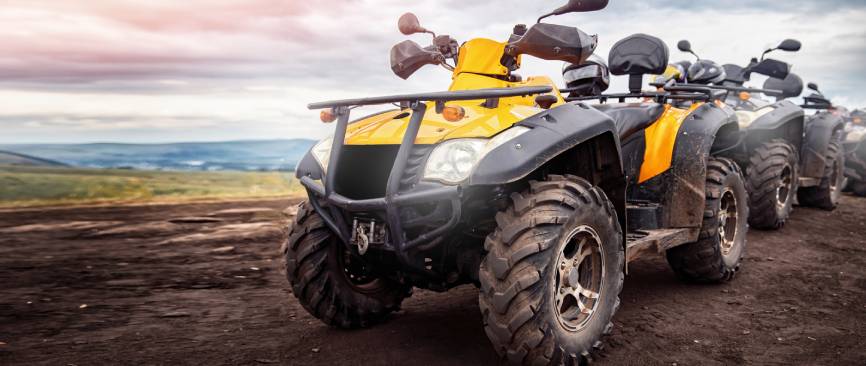 3 ATVs aligned in an outdoor muddy landscape with headlights on in a cloudy day with muddy tires ready for adventur