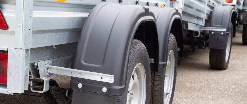 A close-up of the tires on one side of a trailer, which is parked among a row of trailers situated in an outdoor environment.