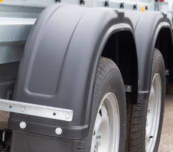A close-up of the tires on one side of a trailer, which is parked among a row of trailers situated in an outdoor environment.