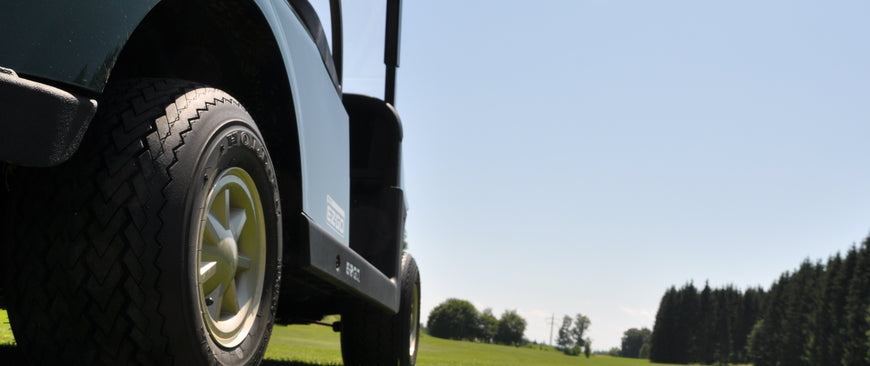 A golf cart parked on a golf course with trees and bushes in the distance and grass that's been freshly cut.