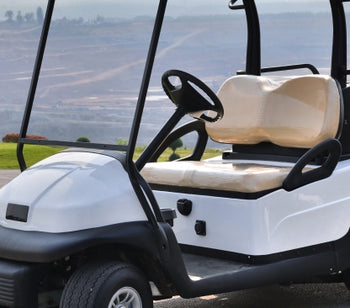 Two white golf carts parked on a section of pavement. There are palm trees and hills in the distance.