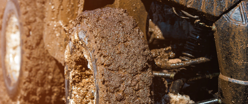 A close up of ATV tires in the mud on the right side. There is mud all over the tires and the ATV.